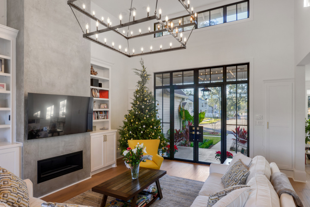 This is an example of a mid-sized modern open concept living room in New Orleans with white walls, light hardwood floors, a standard fireplace, a concrete fireplace surround, a wall-mounted tv and brown floor.