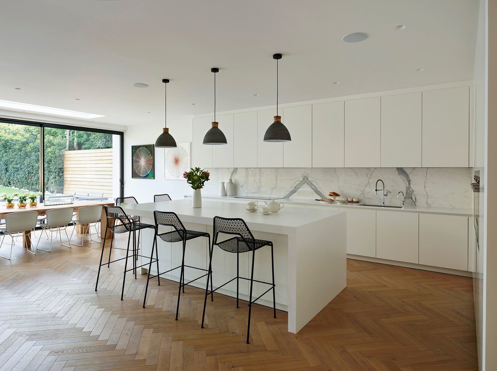 Photo of a contemporary eat-in kitchen in London with an undermount sink, flat-panel cabinets, white splashback, marble splashback, light hardwood floors, with island and beige floor.