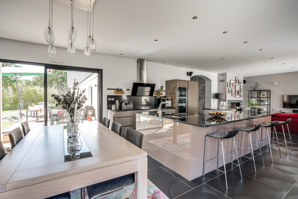 Large contemporary u-shaped open plan kitchen with an undermount sink, flat-panel cabinets, brown cabinets, granite benchtops, black splashback, ceramic floors, with island, black floor and black benchtop.