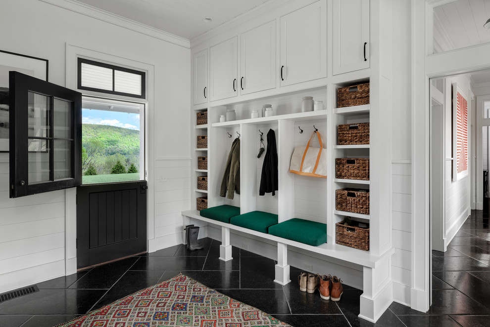 Large country mudroom in New York with white walls, a dutch front door, a black front door and black floor.