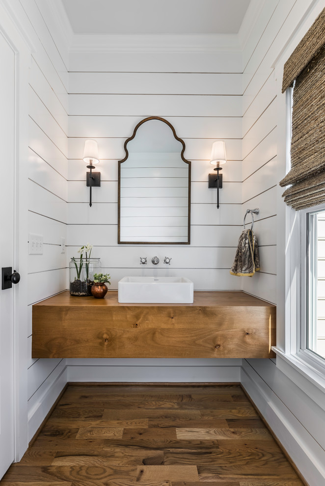 This is an example of a small country powder room in Other with white walls, medium hardwood floors, a vessel sink, wood benchtops, brown benchtops, brown floor, flat-panel cabinets and medium wood cabinets.