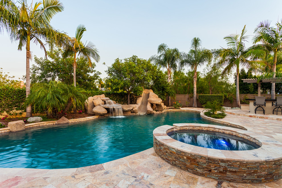 This is an example of a large tropical backyard custom-shaped pool in San Diego with natural stone pavers and a water slide.