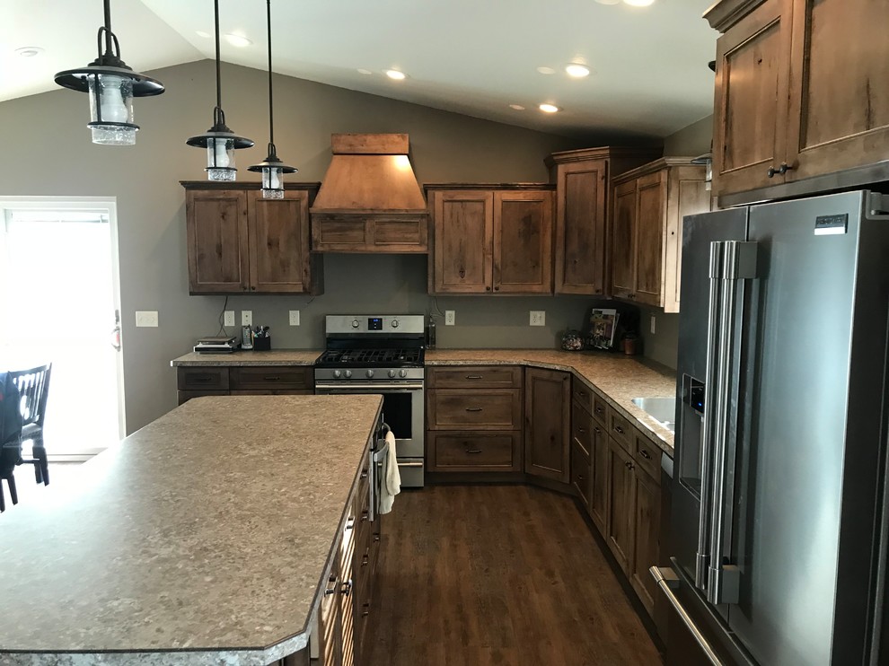 Large mountain style l-shaped medium tone wood floor and brown floor kitchen photo with an undermount sink, recessed-panel cabinets, medium tone wood cabinets, stainless steel appliances, an island and laminate countertops
