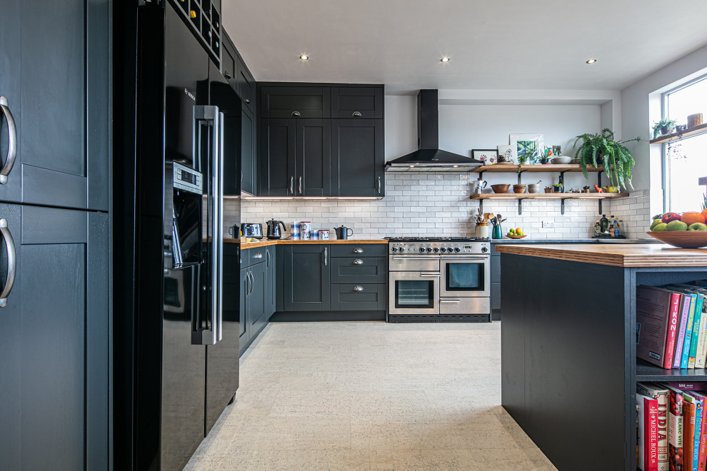 Photo of a large urban kitchen/diner in Other with shaker cabinets, blue cabinets, stainless steel worktops, white splashback, metro tiled splashback, stainless steel appliances, cork flooring, a breakfast bar and white floors.