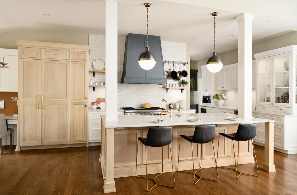 Large transitional l-shaped medium tone wood floor and brown floor kitchen photo in New York with a farmhouse sink, light wood cabinets, white backsplash, stainless steel appliances, an island, white countertops and shaker cabinets
