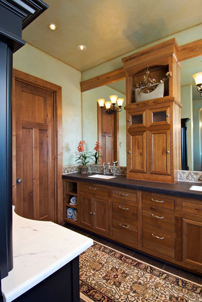Inspiration for a large traditional master bathroom in Other with recessed-panel cabinets, dark wood cabinets, green walls, porcelain floors, an undermount sink, soapstone benchtops, brown floor and black benchtops.