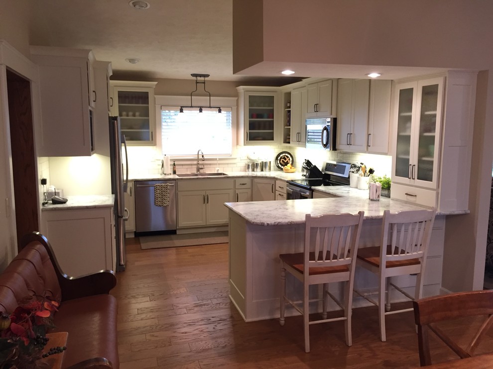 Example of a mid-sized transitional u-shaped medium tone wood floor eat-in kitchen design with an integrated sink, shaker cabinets, white cabinets, laminate countertops, white backsplash, subway tile backsplash, stainless steel appliances and a peninsula