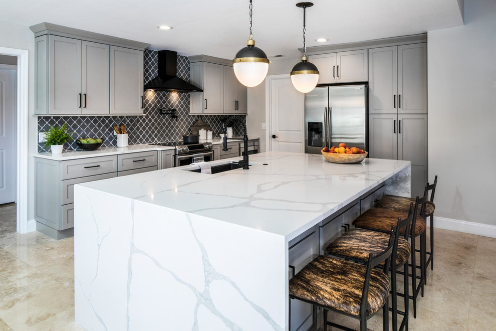 Large modern l-shaped kitchen in Tampa with an undermount sink, shaker cabinets, grey cabinets, quartz benchtops, grey splashback, glass tile splashback, stainless steel appliances, travertine floors, with island, beige floor and white benchtop.
