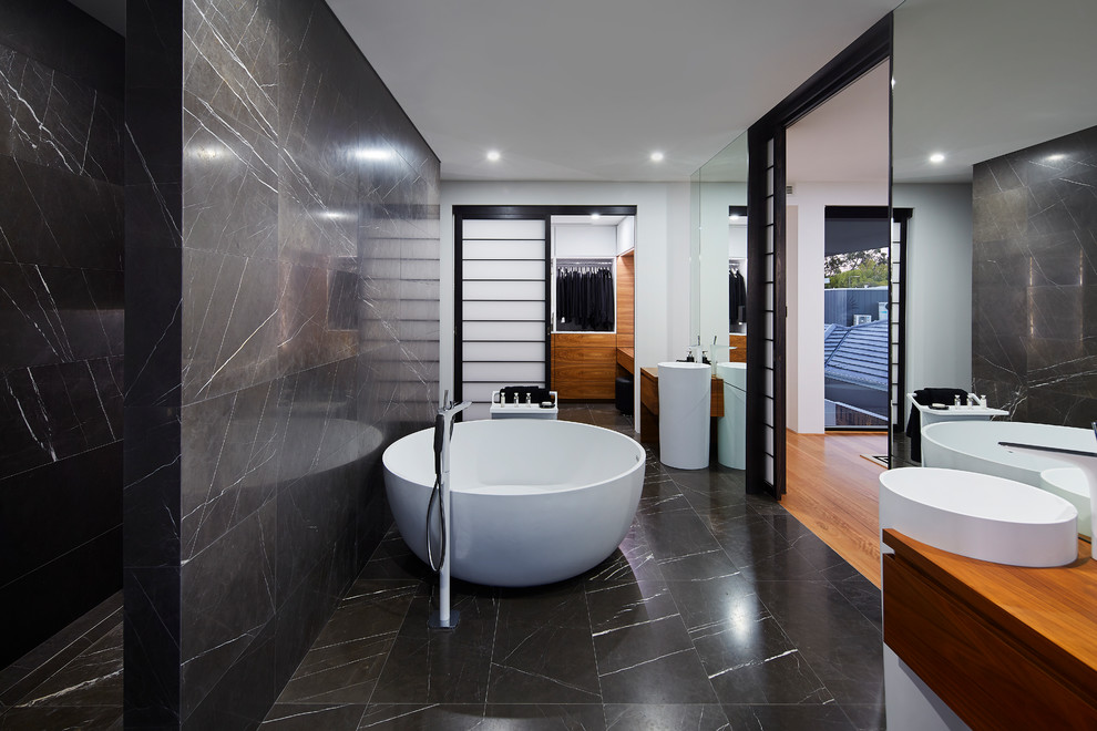 Inspiration for a master bathroom in Perth with flat-panel cabinets, medium wood cabinets, a freestanding tub, black tile, white walls, a pedestal sink, black floor and an open shower.