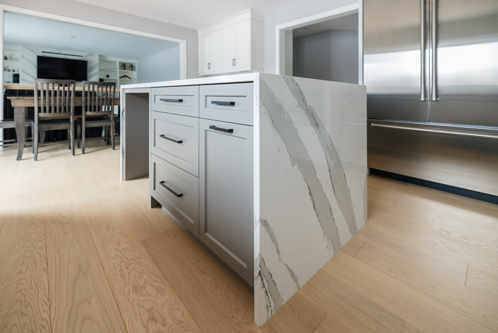 Mid-sized transitional u-shaped light wood floor eat-in kitchen photo in Toronto with an undermount sink, shaker cabinets, white cabinets, quartz countertops, white backsplash, quartz backsplash, stainless steel appliances, an island and white countertops