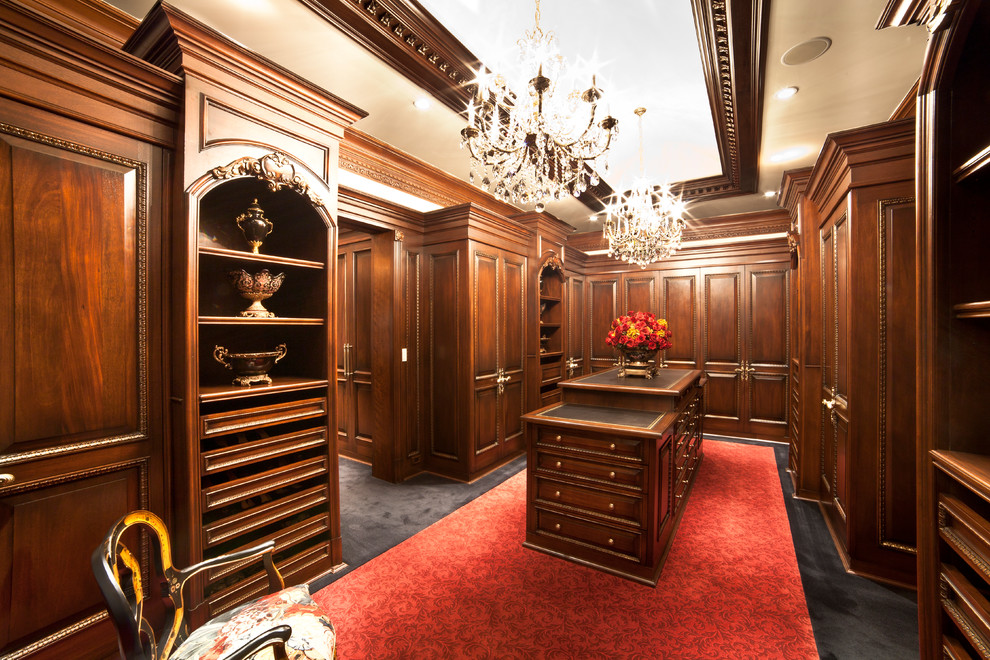 Inspiration for a mid-sized traditional gender-neutral walk-in wardrobe in New York with raised-panel cabinets, dark wood cabinets and carpet.