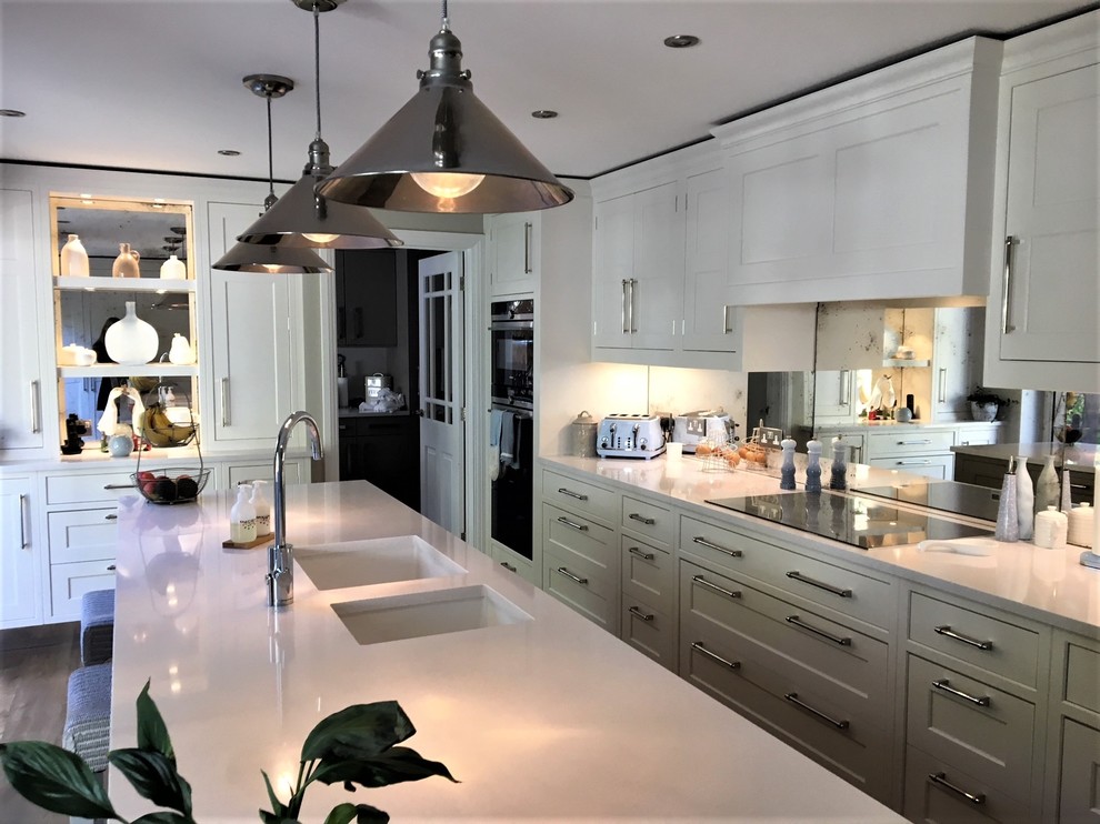 This is an example of a mid-sized traditional l-shaped eat-in kitchen in Surrey with a double-bowl sink, shaker cabinets, white cabinets, onyx benchtops, mirror splashback, black appliances, porcelain floors, with island, multi-coloured floor and white benchtop.