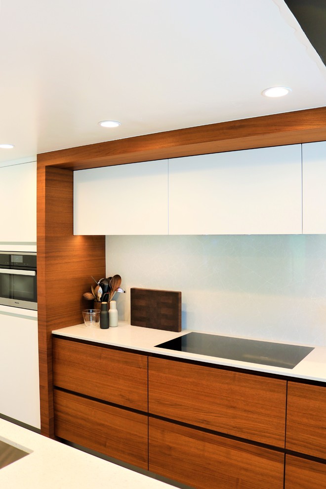 This is an example of a contemporary kitchen in Orange County with flat-panel cabinets, light wood cabinets, quartz benchtops, white splashback, white benchtop, a single-bowl sink, black appliances, concrete floors and grey floor.
