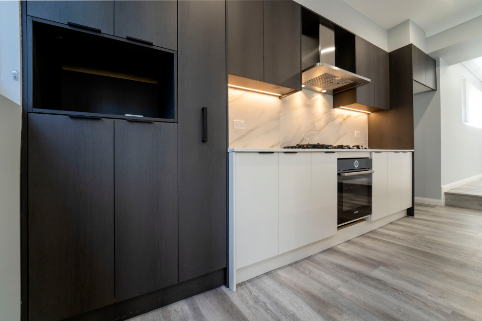 This is an example of a large contemporary galley open plan kitchen in Sydney with a drop-in sink, flat-panel cabinets, black cabinets, quartz benchtops, multi-coloured splashback, marble splashback, black appliances, laminate floors, with island, grey floor and white benchtop.