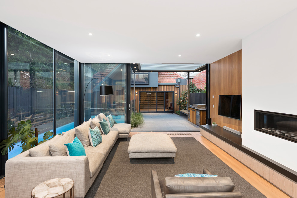Design ideas for a contemporary open concept living room in Melbourne with white walls, medium hardwood floors, a ribbon fireplace, a wall-mounted tv and brown floor.