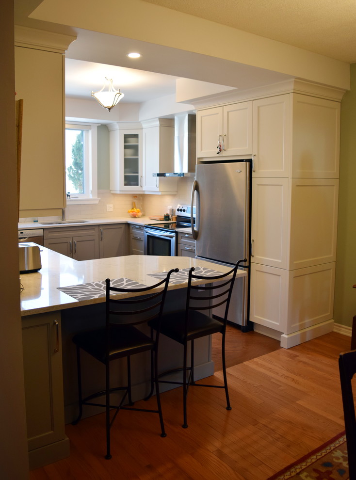 Eat-in kitchen - mid-sized transitional l-shaped medium tone wood floor eat-in kitchen idea in Toronto with an undermount sink, shaker cabinets, white cabinets, quartz countertops, white backsplash, subway tile backsplash, stainless steel appliances and a peninsula