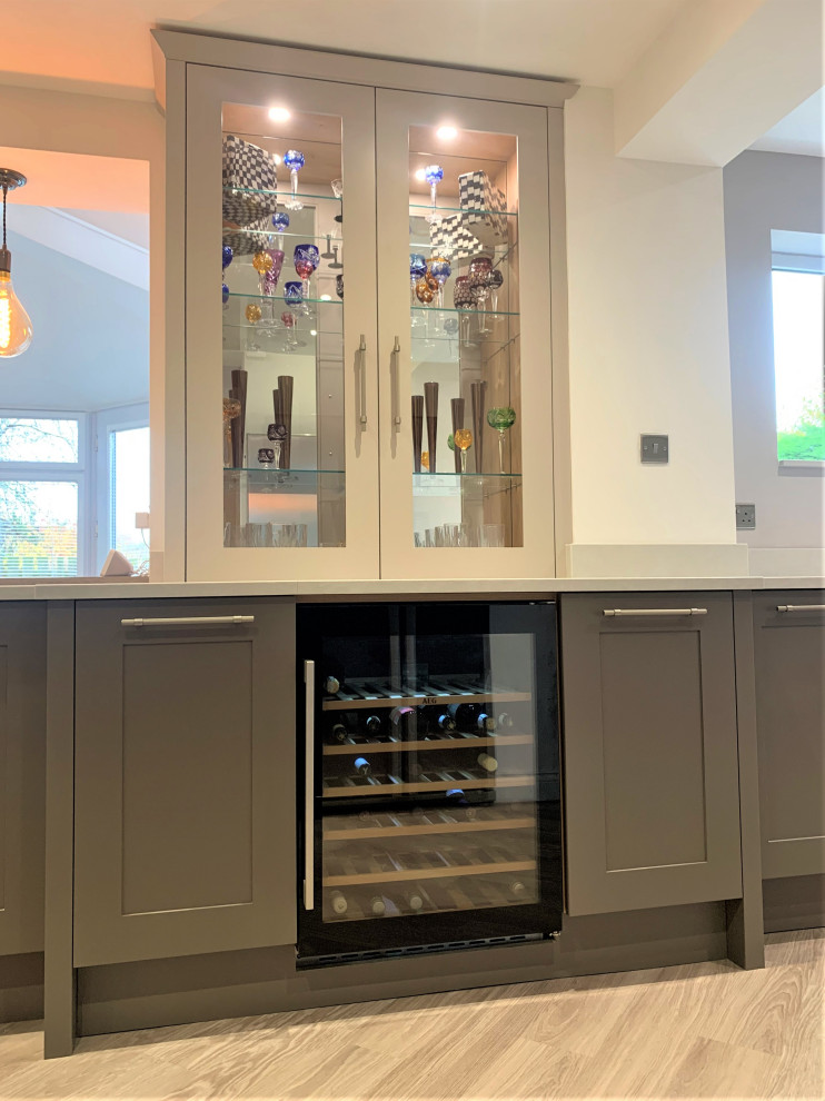 Photo of a mid-sized traditional u-shaped home bar in Other with shaker cabinets, quartzite benchtops, glass sheet splashback, vinyl floors and white benchtop.