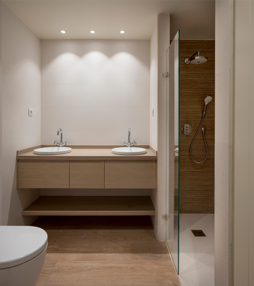 Design ideas for a mid-sized transitional master bathroom in Bilbao with flat-panel cabinets, a curbless shower, a wall-mount toilet, white tile, ceramic tile, laminate floors, a vessel sink, brown floor, a hinged shower door, white cabinets, grey walls, engineered quartz benchtops and brown benchtops.