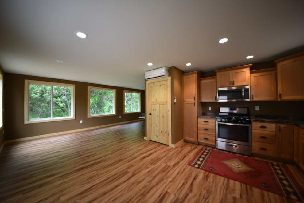 Inspiration for a mid-sized rustic l-shaped laminate floor and brown floor eat-in kitchen remodel in Minneapolis with a drop-in sink, flat-panel cabinets, light wood cabinets, granite countertops, black backsplash, stainless steel appliances and no island