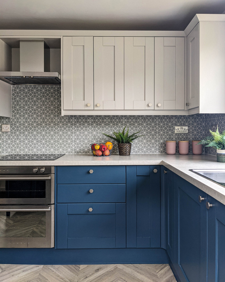 Bild på ett stort maritimt grå grått kök, med en integrerad diskho, skåp i shakerstil, blå skåp, laminatbänkskiva, grått stänkskydd, stänkskydd i keramik, svarta vitvaror, laminatgolv och en köksö