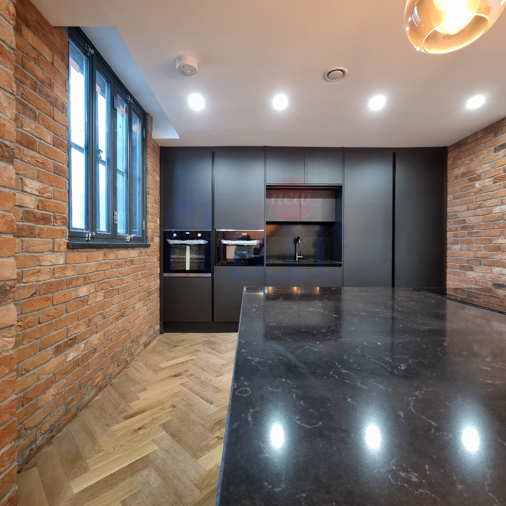This is an example of a large single-wall open plan kitchen in West Midlands with an integrated sink, black cabinets, quartz worktops, black splashback, white appliances, light hardwood flooring, an island, brown floors, black worktops, a coffered ceiling and feature lighting.