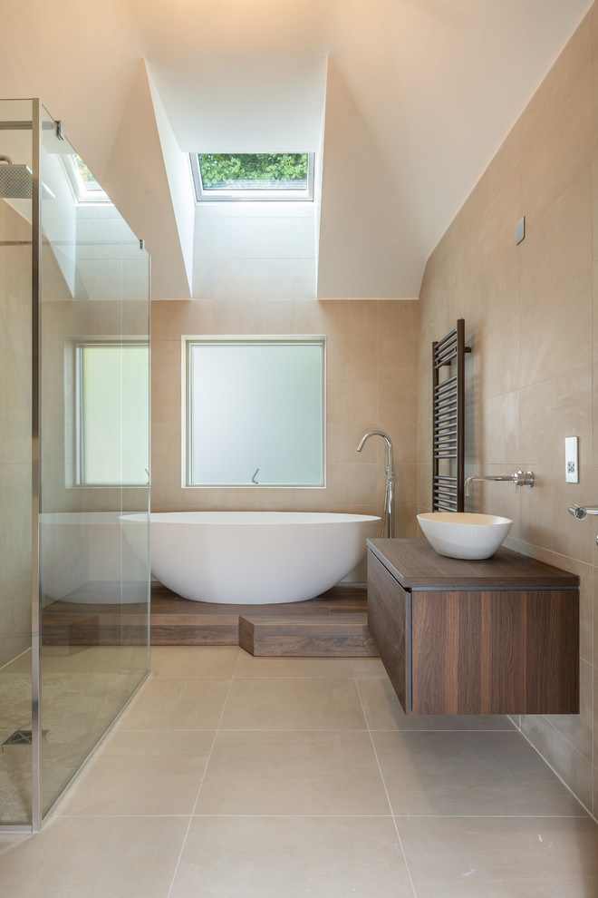 Photo of a modern master bathroom in Manchester with flat-panel cabinets, dark wood cabinets, a freestanding tub, a curbless shower, beige tile, beige walls, a vessel sink, wood benchtops, beige floor, an open shower and brown benchtops.