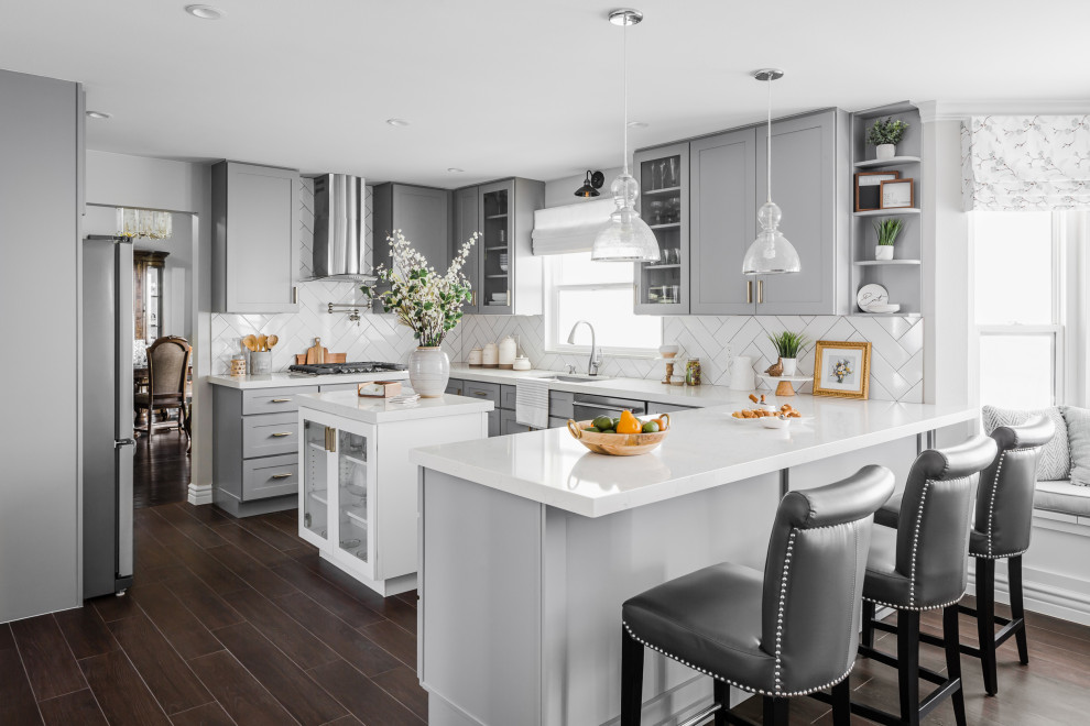 Transitional u-shaped kitchen in Los Angeles with an undermount sink, shaker cabinets, grey cabinets, white splashback, stainless steel appliances, dark hardwood floors, with island, brown floor and white benchtop.