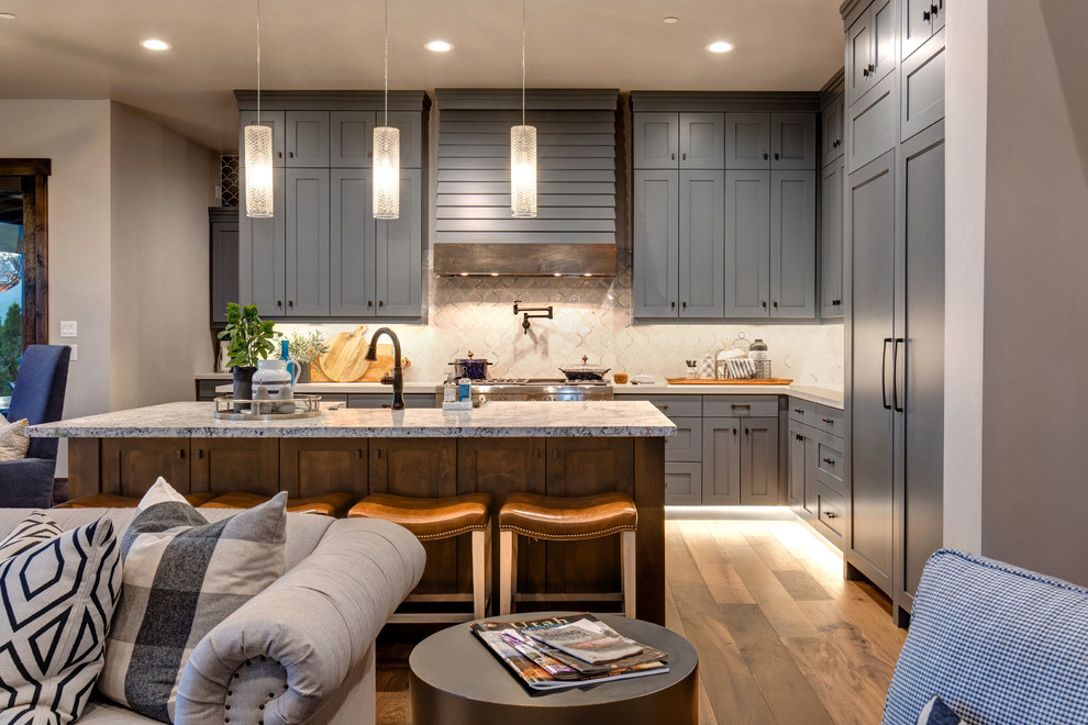 This is an example of a traditional l-shaped open plan kitchen in Salt Lake City with a drop-in sink, recessed-panel cabinets, grey cabinets, granite benchtops, white splashback, ceramic splashback, stainless steel appliances, medium hardwood floors, with island and white benchtop.