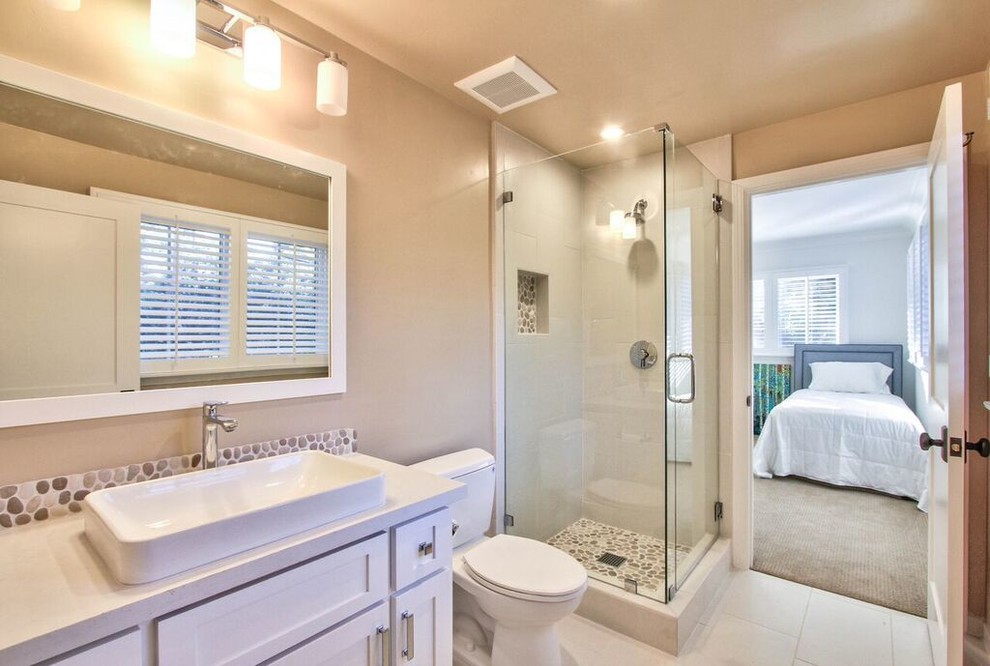 This is an example of a small transitional bathroom in Los Angeles with furniture-like cabinets, white cabinets, a corner shower, a two-piece toilet, beige walls, a vessel sink, white floor, a hinged shower door and white benchtops.