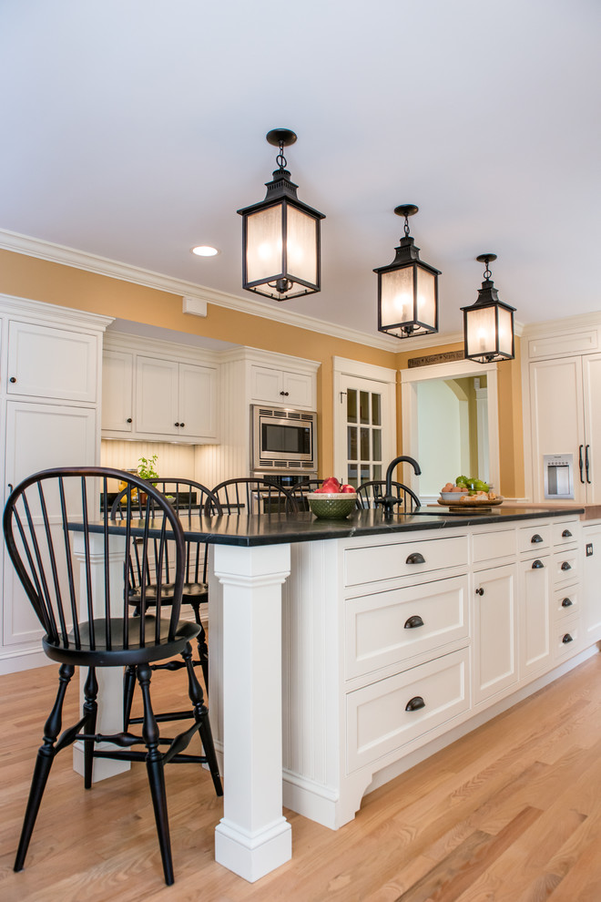 This is an example of a mid-sized transitional u-shaped eat-in kitchen in Portland Maine with an undermount sink, shaker cabinets, white cabinets, stainless steel appliances, bamboo floors and with island.