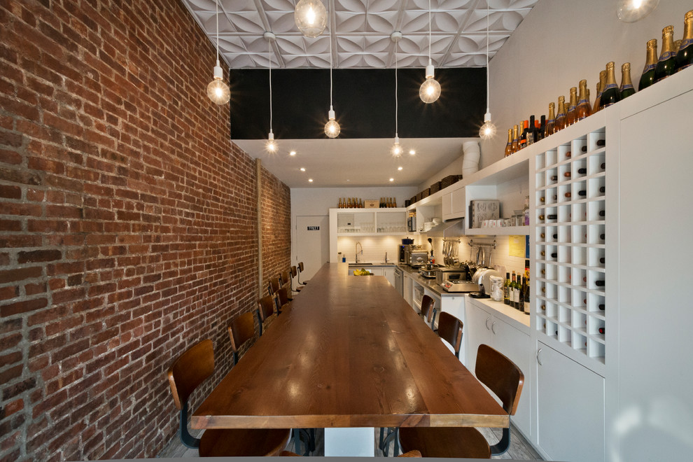 Example of a trendy eat-in kitchen design in New York with a double-bowl sink, flat-panel cabinets, white cabinets, white backsplash, subway tile backsplash, stainless steel appliances and an island
