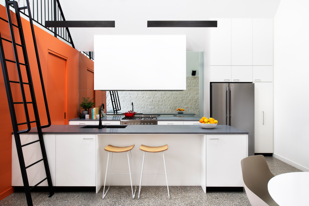 Inspiration for a mid-sized contemporary galley eat-in kitchen in Sydney with a double-bowl sink, flat-panel cabinets, white cabinets, mirror splashback, stainless steel appliances, concrete floors, with island, black benchtop and vaulted.