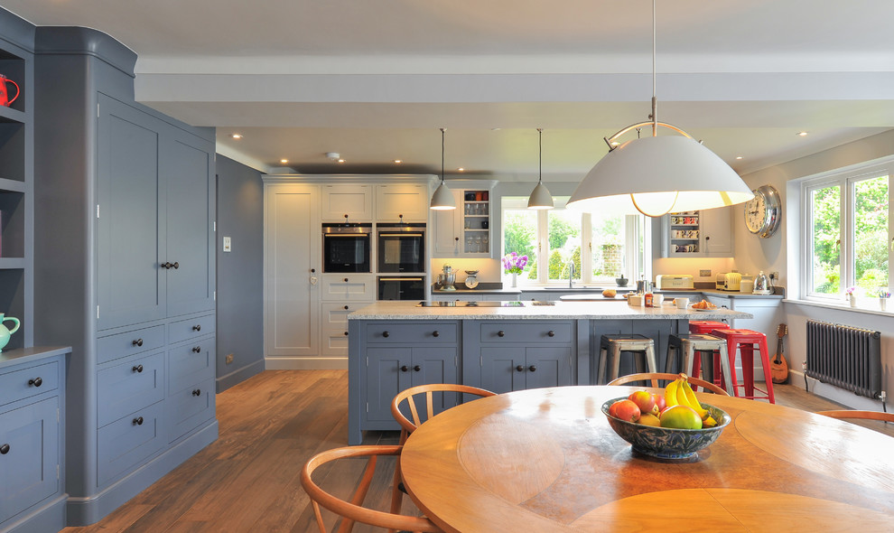 Photo of a large contemporary open plan kitchen in Hampshire with a drop-in sink, blue cabinets, granite benchtops, black appliances, ceramic floors and with island.