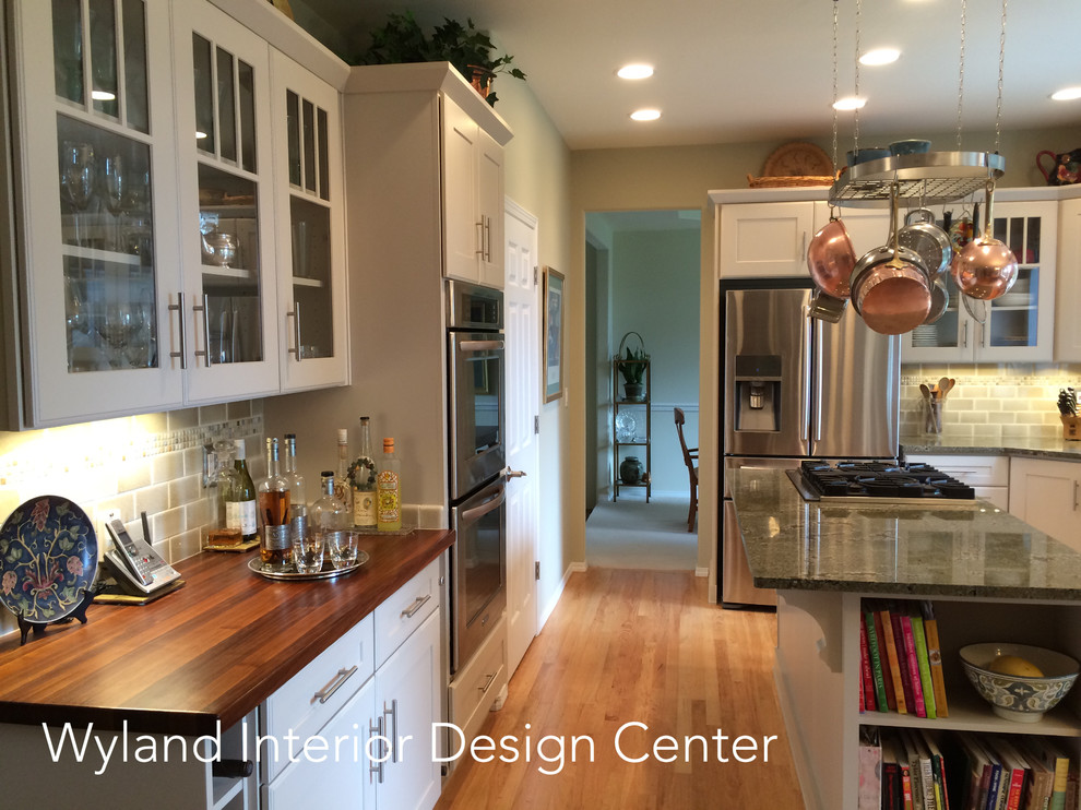 This is an example of a mid-sized country u-shaped eat-in kitchen in Seattle with a farmhouse sink, shaker cabinets, beige cabinets, granite benchtops, beige splashback, ceramic splashback, stainless steel appliances, light hardwood floors and with island.