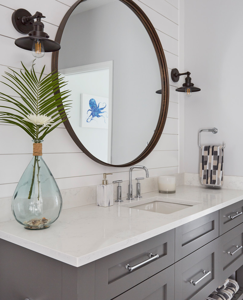 This is an example of a mid-sized beach style 3/4 bathroom in Other with shaker cabinets, grey cabinets, an alcove shower, a two-piece toilet, white tile, wood-look tile, white walls, wood-look tile, a wall-mount sink, engineered quartz benchtops, grey floor, a hinged shower door, grey benchtops, a single vanity and a freestanding vanity.