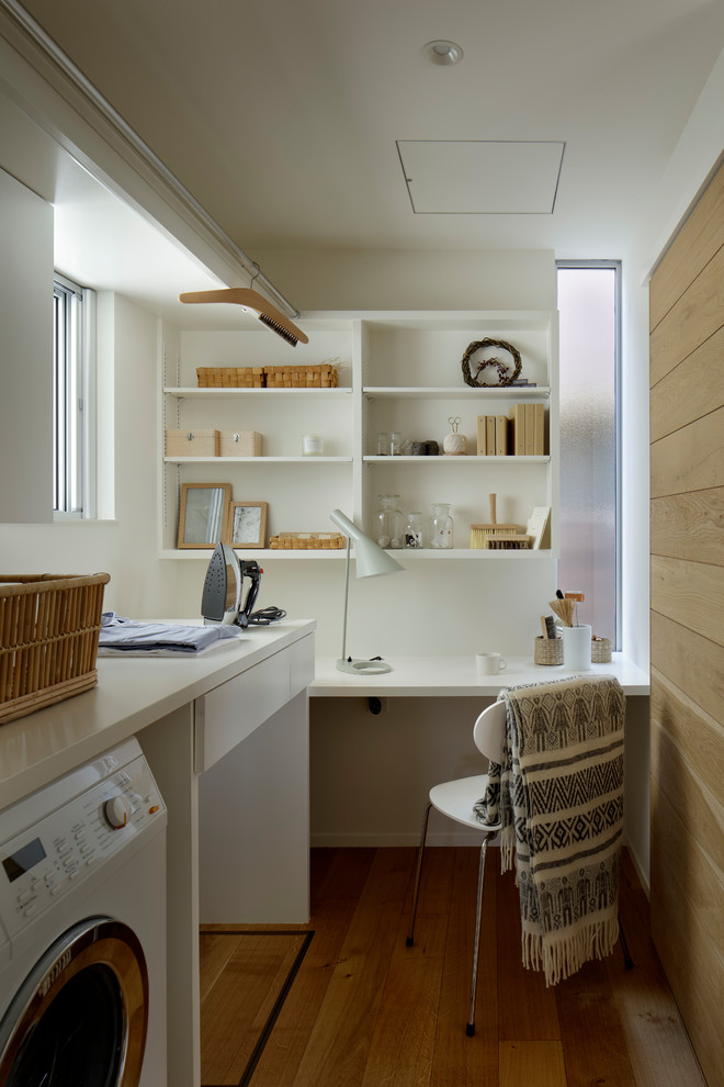 Inspiration for a small scandinavian l-shaped utility room in Other with white walls, open cabinets, white cabinets, medium hardwood floors, brown floor and white benchtop.