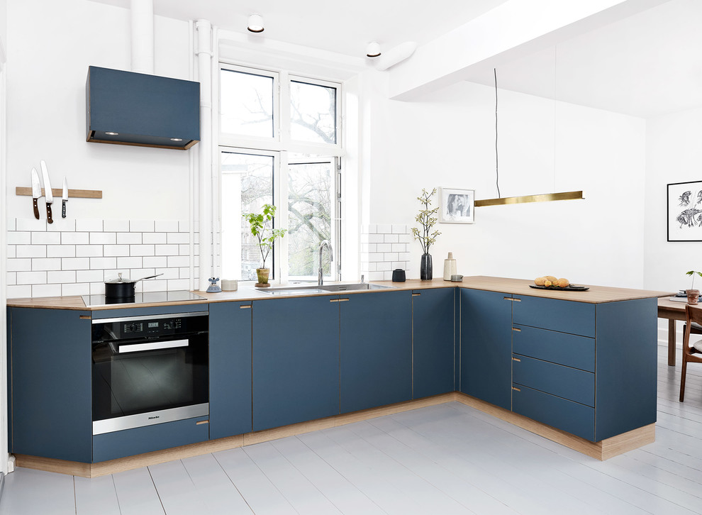 Mid-sized scandinavian l-shaped eat-in kitchen in Copenhagen with a drop-in sink, beaded inset cabinets, blue cabinets, wood benchtops, white splashback, ceramic splashback, stainless steel appliances, painted wood floors, a peninsula and white floor.