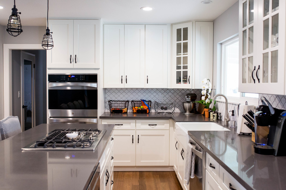 Example of a mid-sized transitional light wood floor eat-in kitchen design in Sacramento with a farmhouse sink, shaker cabinets, white cabinets, white backsplash, glass tile backsplash, stainless steel appliances and an island