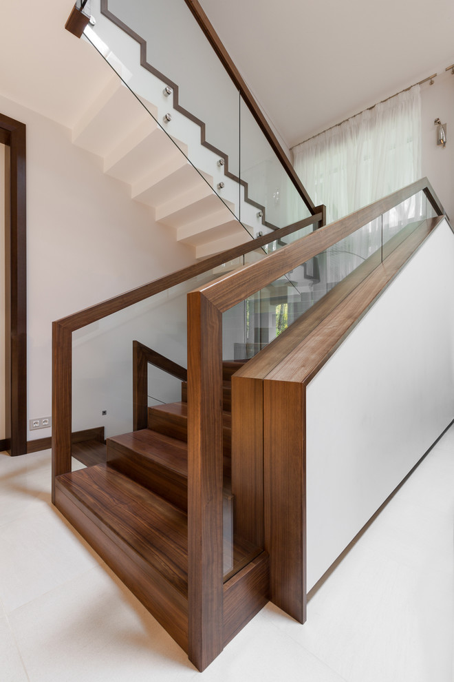 Photo of a large contemporary wood u-shaped staircase in Other with wood risers and glass railing.