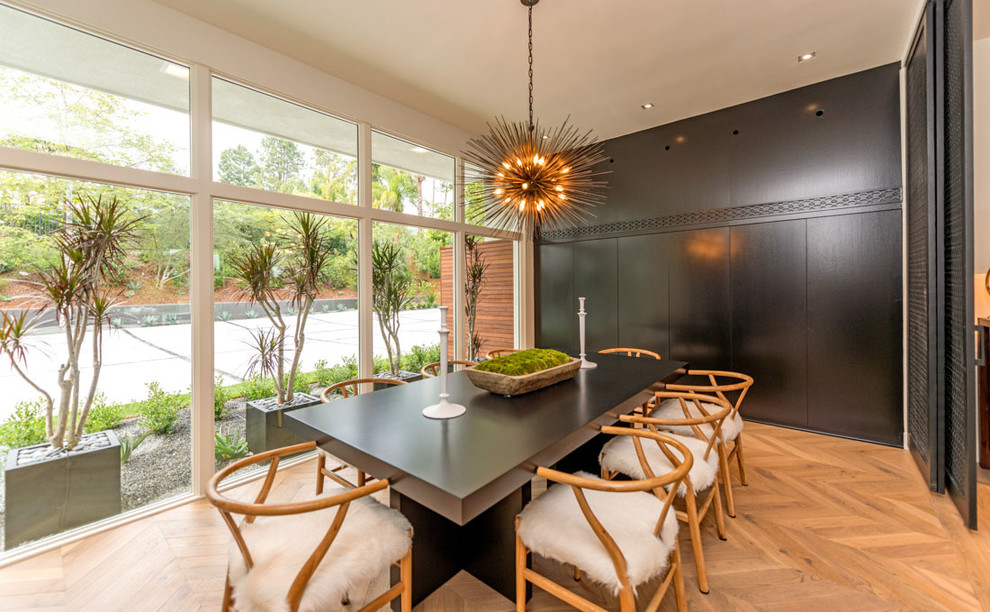 This is an example of a midcentury dining room in Los Angeles with black walls, light hardwood floors and beige floor.