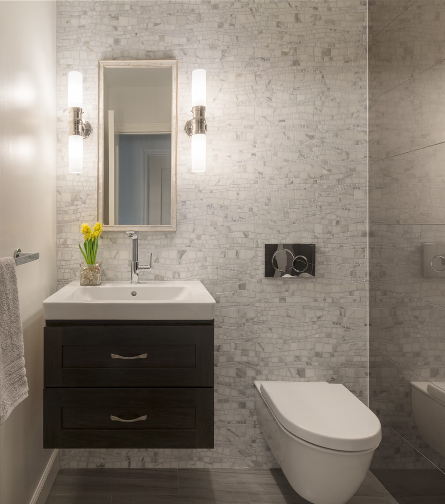Photo of a transitional powder room in San Francisco with flat-panel cabinets, grey cabinets, a wall-mount toilet, gray tile, porcelain tile, beige walls, a wall-mount sink and grey floor.