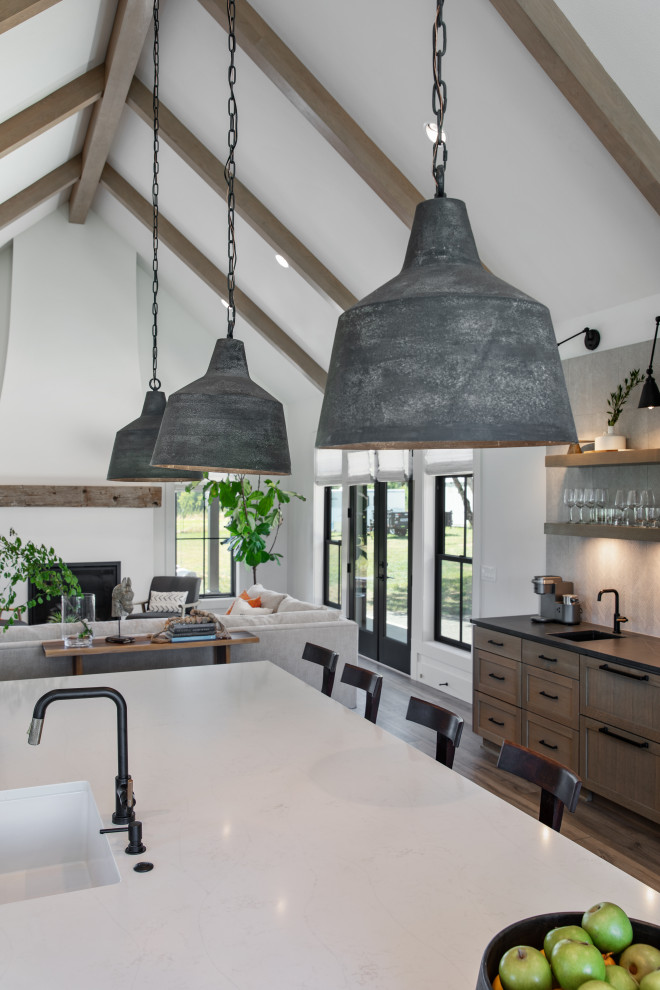 This is an example of an expansive country galley eat-in kitchen in Portland with a farmhouse sink, shaker cabinets, white cabinets, quartz benchtops, white splashback, mosaic tile splashback, stainless steel appliances, vinyl floors, with island, brown floor, white benchtop and exposed beam.