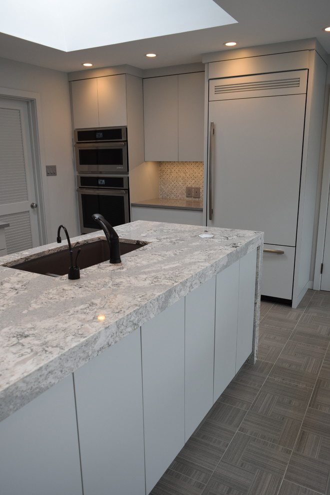 Example of a minimalist ceramic tile and gray floor kitchen design with an undermount sink, flat-panel cabinets, gray cabinets, quartz countertops, multicolored backsplash, glass tile backsplash, paneled appliances, an island and gray countertops