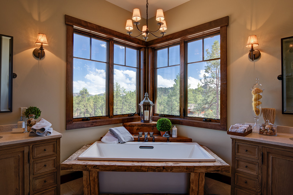 Example of a huge mountain style master beige tile medium tone wood floor freestanding bathtub design in Phoenix with furniture-like cabinets, dark wood cabinets, beige walls, an integrated sink and granite countertops