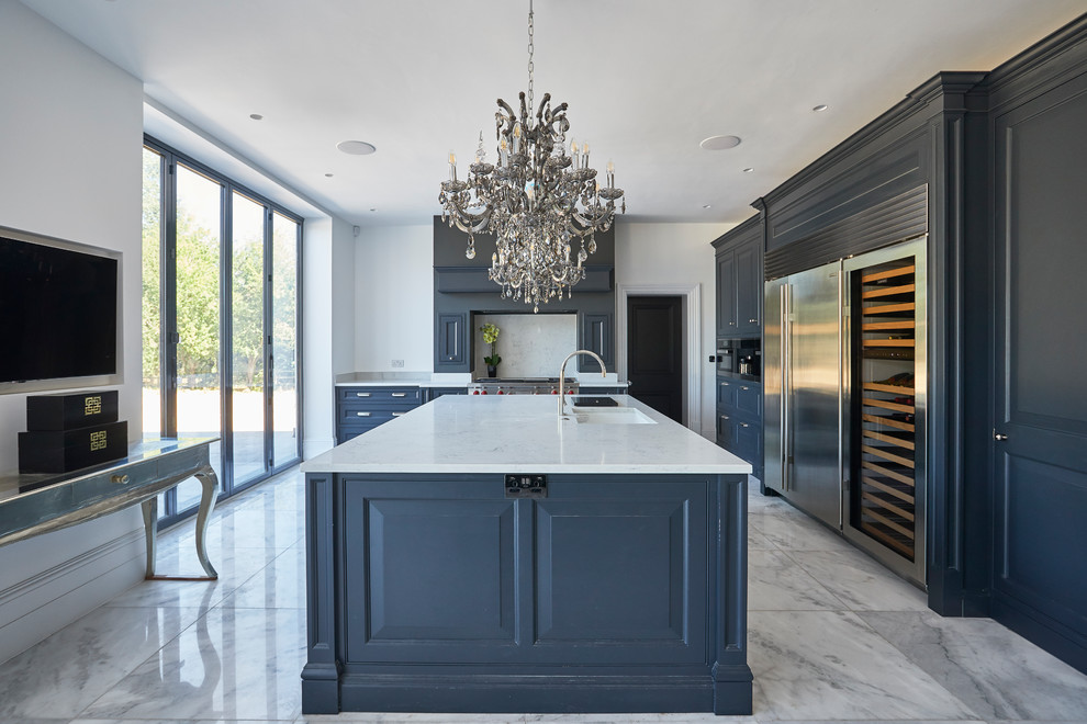 Transitional l-shaped kitchen in Other with an undermount sink, raised-panel cabinets, blue cabinets, white splashback, stone slab splashback, stainless steel appliances, with island, grey floor and white benchtop.