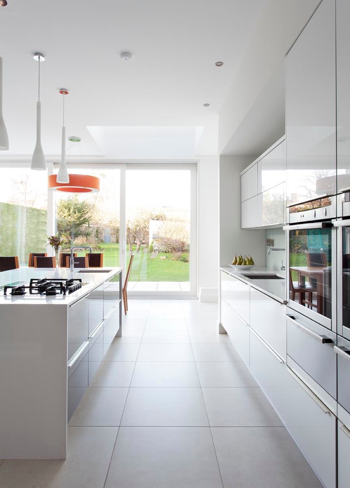 Expansive contemporary open plan kitchen in Dublin with flat-panel cabinets, white cabinets, quartz benchtops, white splashback, glass sheet splashback, stainless steel appliances, porcelain floors, with island and an undermount sink.
