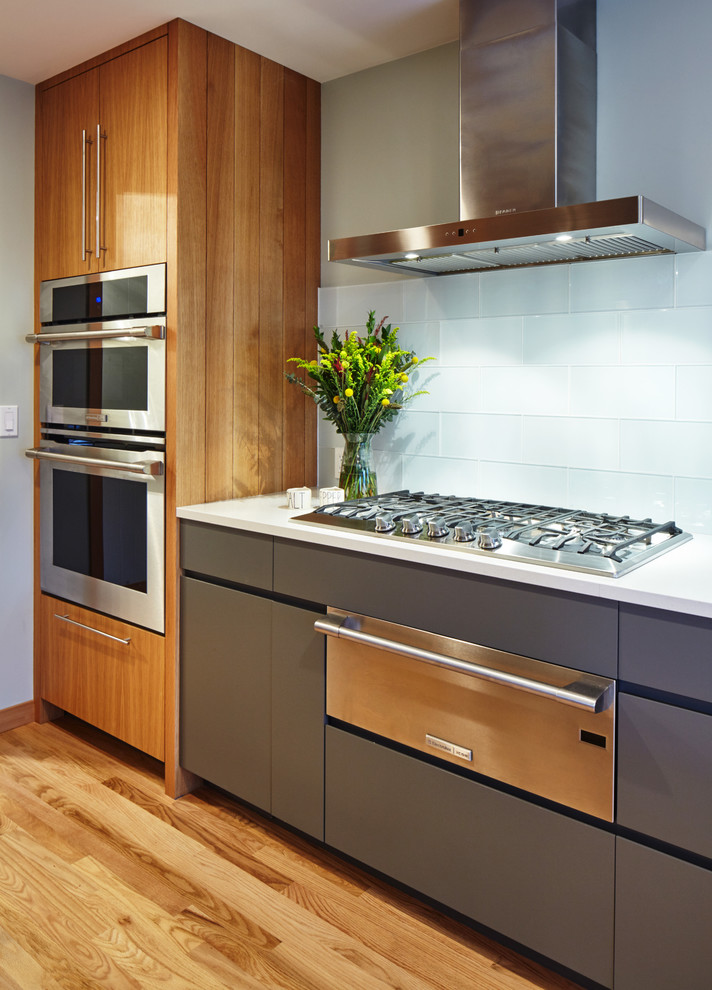 This is an example of a contemporary galley eat-in kitchen in Portland with a drop-in sink, flat-panel cabinets, grey cabinets, quartz benchtops, white splashback, glass tile splashback, stainless steel appliances, medium hardwood floors and a peninsula.