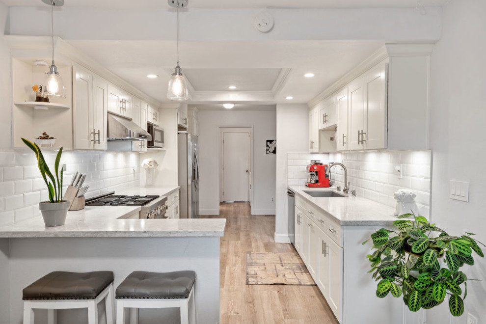 Inspiration for a small transitional galley separate kitchen in San Francisco with an undermount sink, shaker cabinets, white cabinets, white splashback, ceramic splashback, stainless steel appliances, laminate floors, a peninsula, grey floor, white benchtop and coffered.