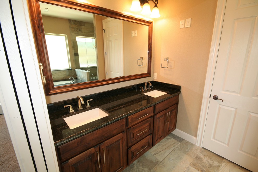Traditional master bathroom in Austin with raised-panel cabinets, dark wood cabinets, a corner tub, a corner shower, a two-piece toilet, beige tile, porcelain tile, beige walls, porcelain floors, an undermount sink, granite benchtops, multi-coloured floor, a hinged shower door and multi-coloured benchtops.