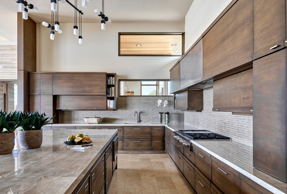This is an example of a large l-shaped open plan kitchen in Phoenix with an undermount sink, flat-panel cabinets, dark wood cabinets, granite benchtops, glass tile splashback, panelled appliances, limestone floors, with island, beige floor, beige benchtop and grey splashback.